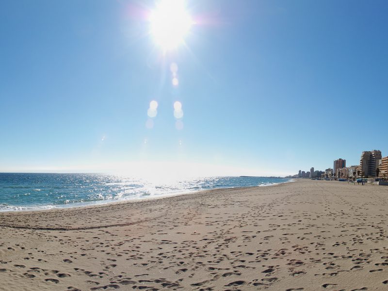 Weiter Sandstrand von Fuengirola unter blauem Himmel, davor das Mittelmeer und entlang der Küste die Häuser des Ortes