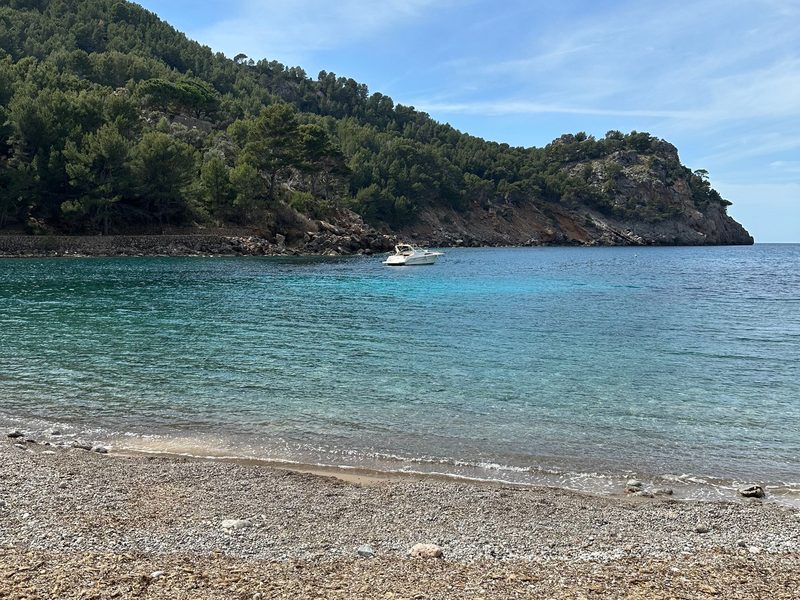 Eine Kiesbucht auf Mallorca zwischen kiefernbewachsenen Felshängen, im türkisen Wasser ankert ein Motorboot — zeigt nicht den genannten Ort
