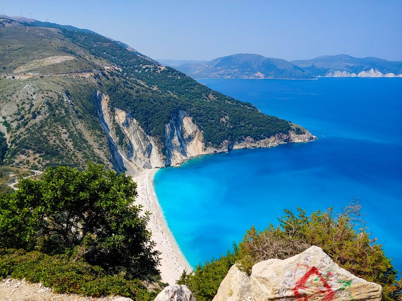 Die Bucht von Myrtos auf Kefalonia von oben: heller Kiesstrand am Fuß steiler weißer Felswände, davor das leuchtend türkise Meer