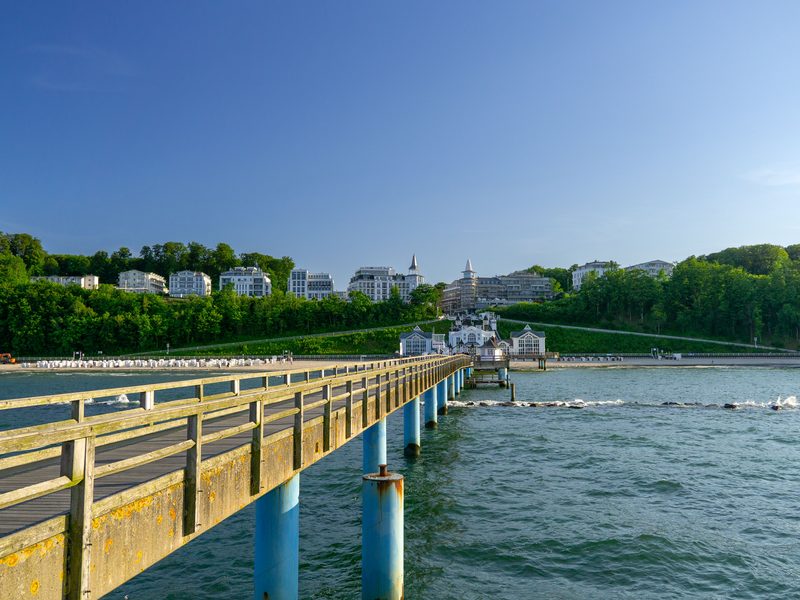 Die Seebrücke Sellin führt auf das Ostseebad zu, mit Kurhäusern der Bäderarchitektur zwischen grünen Hängen — zeigt nicht den genannten Ort