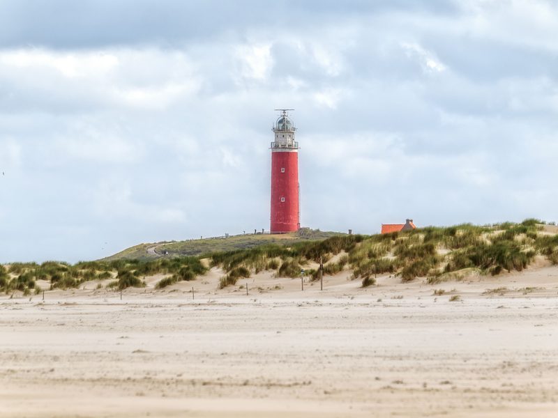 Der rote Leuchtturm Eierland am Nordende von Texel, davor der breite Sandstrand und ein Dünenkamm mit Strandhafer