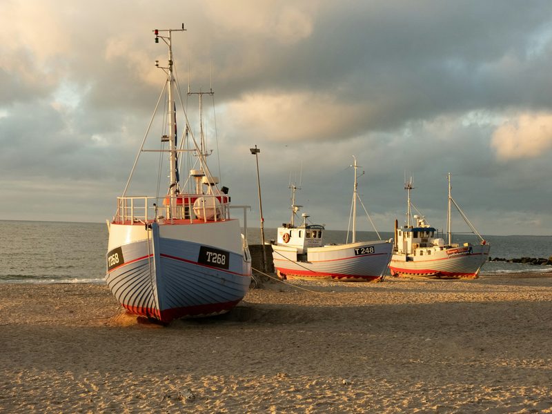 Drei dänische Fischkutter liegen im Abendlicht auf dem Sandstrand von Thisted, im Hintergrund die Nordsee — zeigt nicht den genannten Ort